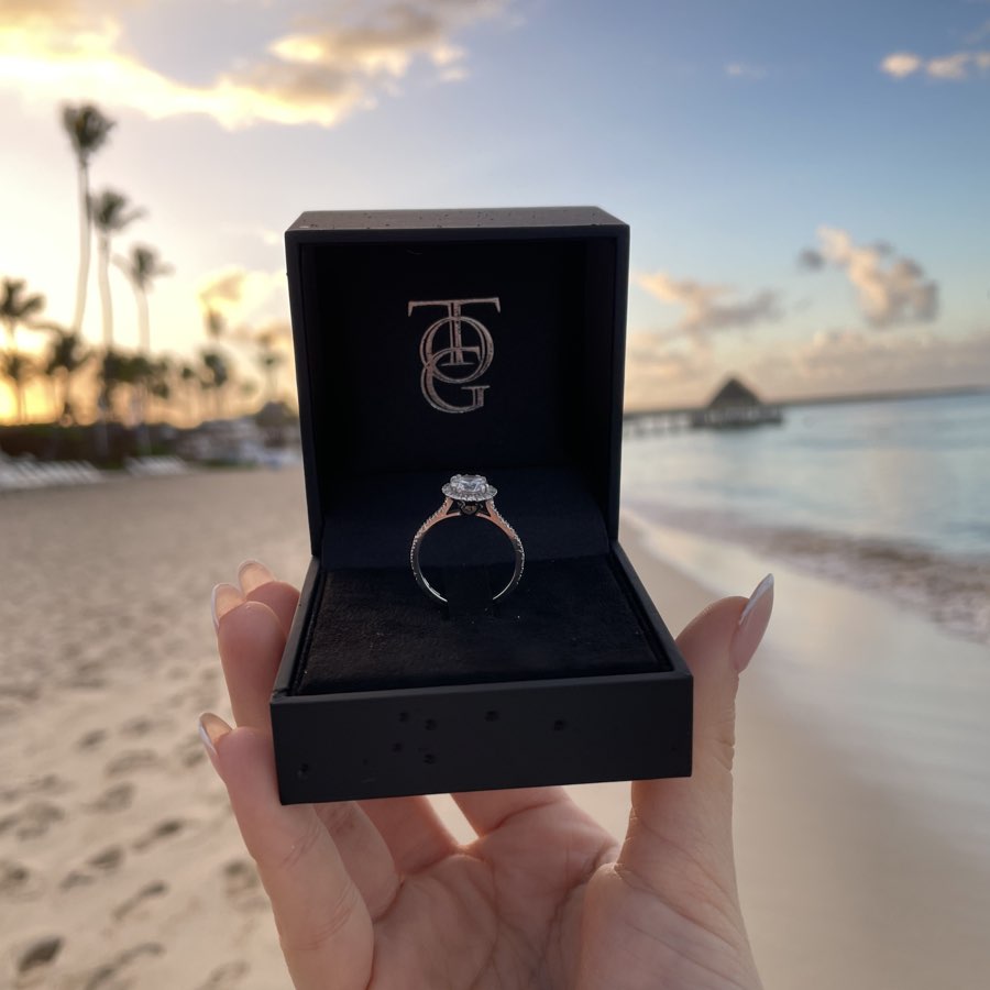 foto di un anello solitario in oro di valenza realizzato da Torinogioielli, fotografato in spiaggia con sullo sfondo un romantico tramonto dai colori stupendi.